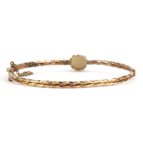 1084 - Victorian 9ct rose gold hinged bangle with safety chain, set with an opal, housed in an antique leat... 