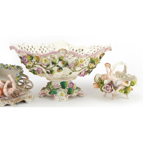 297 - German floral encrusted porcelain including a centrepiece and four footed basket with Putti, the lar... 