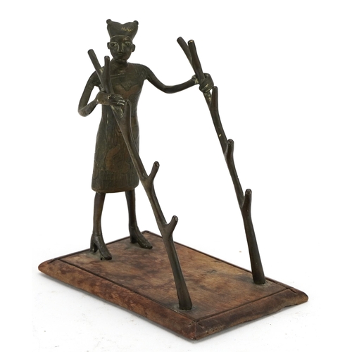 488 - Tribal interest bronze pen-rest on hardwood stand in the form of a tribesman holding two trunks, 16.... 