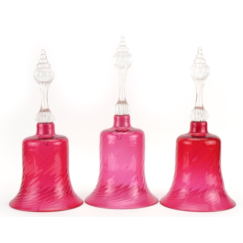 99 - Three Victorian cranberry glass bells, the largest 33cm high