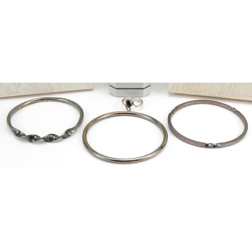 2627 - Jon & Valerie Hill, three silver bangles and silver ring set with cabochon black stone, each housed ... 