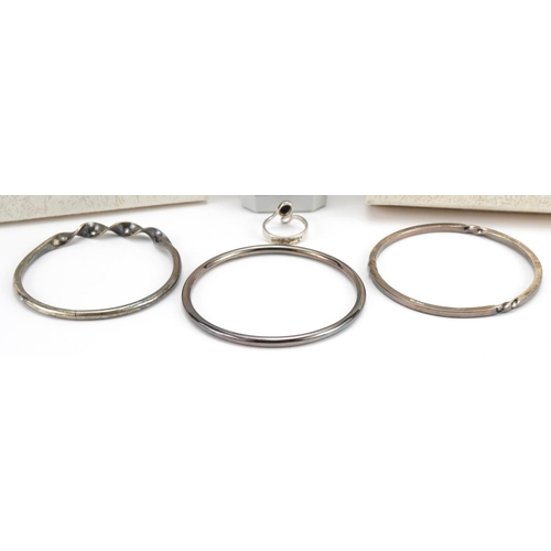 2627 - Jon & Valerie Hill, three silver bangles and silver ring set with cabochon black stone, each housed ... 