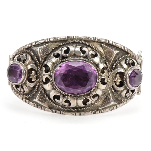 2570 - Antique unmarked silver and amethyst hinged bangle with pierced and embossed decoration, 6.7cm wide