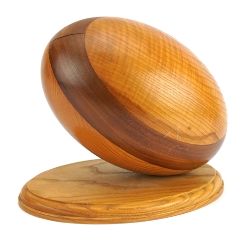 1200 - Wooden sculpture of an American football raised on an oval plinth base, 27cm wide x 24cm high