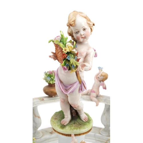 277 - Italian Naples porcelain centrepiece in the form of Putti standing on a pillar surrounded by a porce... 