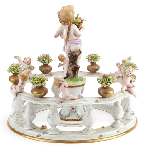 277 - Italian Naples porcelain centrepiece in the form of Putti standing on a pillar surrounded by a porce... 