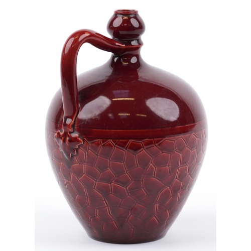 90 - Manner of Bermantofts, Arts & Crafts handled flagon having a red glaze, incised marks and numbers to... 