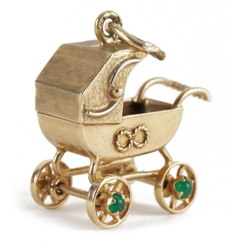 2103 - 9ct gold pram charm with rotating wheels set with cabochon emeralds, 2.4cm high, 3.6g