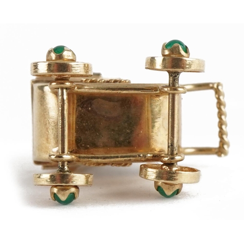 2103 - 9ct gold pram charm with rotating wheels set with cabochon emeralds, 2.4cm high, 3.6g