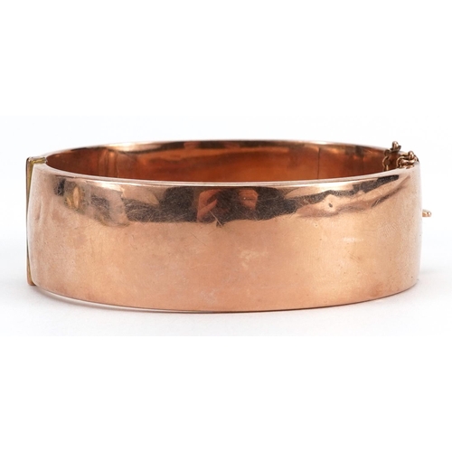 2058 - 9ct rose gold hinged bangle with engraved floral decoration and safety chain, 6.3cm wide, 20.1g