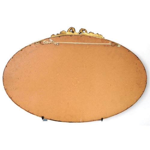 1083 - Oval gilt framed wall hanging mirror with bow crest and bevelled glass, 73cm x 48cm