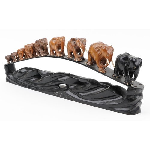 298 - African ebony stand surmounted with nine graduated hardwood elephants, the stand inlaid Ceylon, 78cm... 