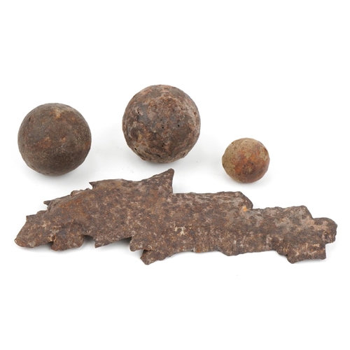 654 - Military interest shrapnel and three cast iron cannon balls, the largest 27.5cm in length