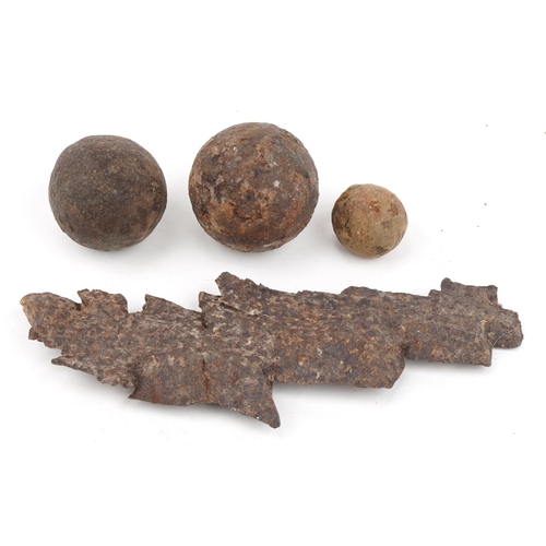 654 - Military interest shrapnel and three cast iron cannon balls, the largest 27.5cm in length