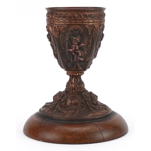 110 - 19th century gilt meta chalice decorated in relief with putti, raised on a circular oak base, with p... 