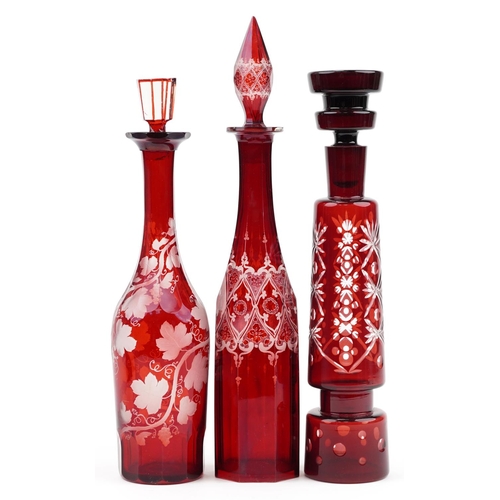 170 - Three Bohemian ruby glass decanters with stoppers including one etched with grapevines, the largest ... 