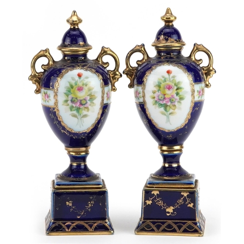 2362 - Pair of Noritake porcelain blue ground vases with twin handles and covers on stands, hand painted wi... 