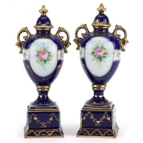 2362 - Pair of Noritake porcelain blue ground vases with twin handles and covers on stands, hand painted wi... 