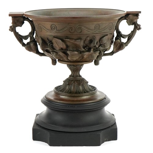 273A - Bronzed Campana urn decorated in relief with flowers and  twin handles, raised on a black slate base... 