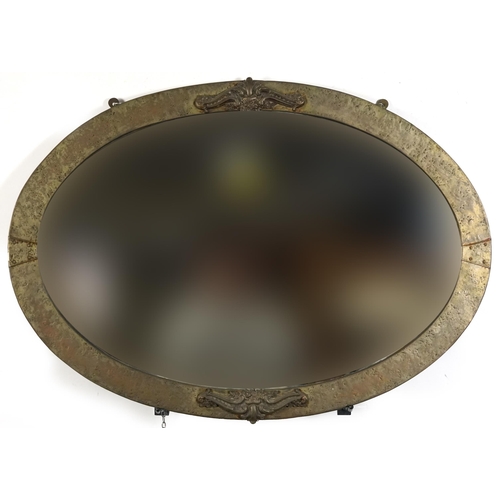 525 - Manner of Liberty & Co, Arts & Crafts style beaten oval wall mirror with bevelled glass, 85.5cm x 61... 