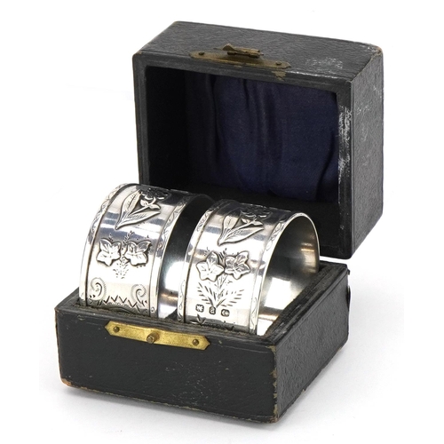 1507 - Pair of Victorian Aeshetic silver napkin rings cast with flowers and foliage housed in a fitted case... 