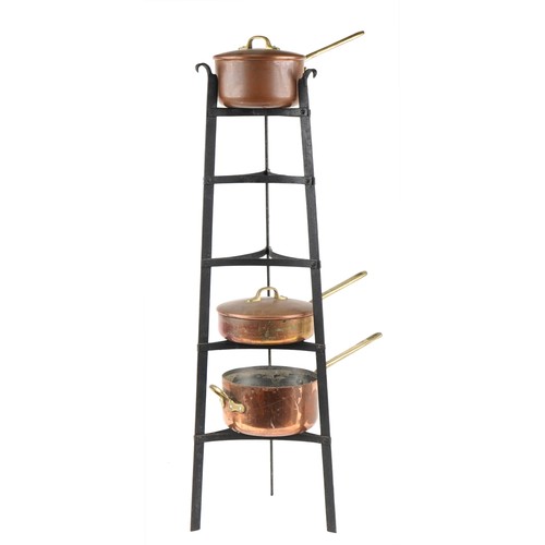 1673 - Three Victorian copper and brass saucepans housed in a tapering wrought cast iron rack