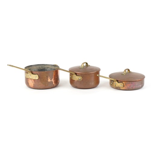 1673 - Three Victorian copper and brass saucepans housed in a tapering wrought cast iron rack