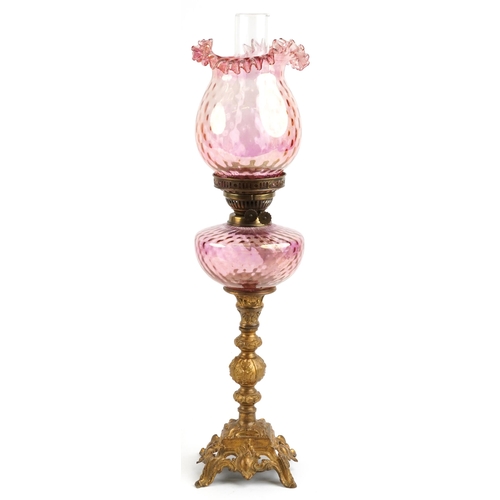 574 - Ornate gilt painted oil lamp with iridescent cranberry glass shade and reservoir, 68.5cm high