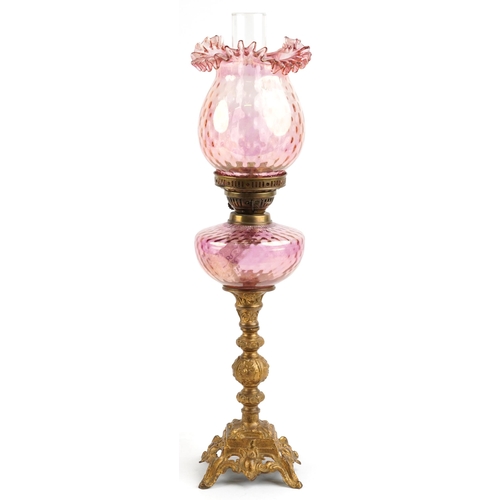 574 - Ornate gilt painted oil lamp with iridescent cranberry glass shade and reservoir, 68.5cm high