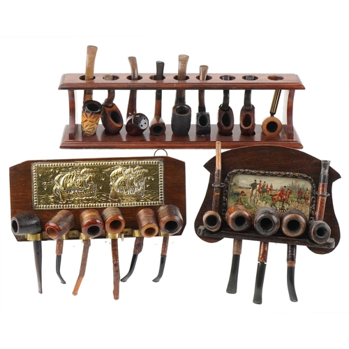 1275 - Twenty vintage tobacco smoking pipes arranged in three pipe racks, two wall hanging, some cherry woo... 