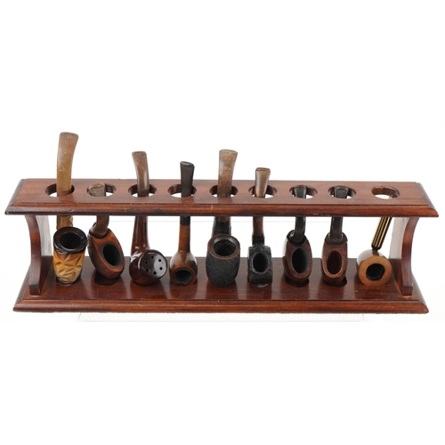 1275 - Twenty vintage tobacco smoking pipes arranged in three pipe racks, two wall hanging, some cherry woo... 