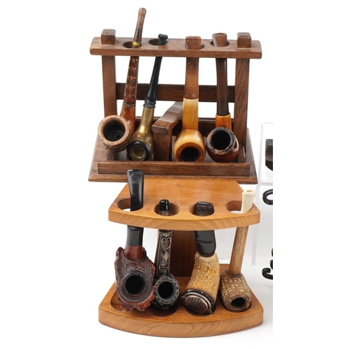 1264 - Twenty one vintage tobacco smoking pipes, some European, arranged in five pipe racks, one carved wit... 