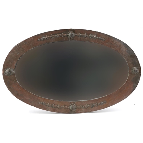 552 - Arts & Crafts beaten copper oval wall mirror with bevelled glass and applied flower heads, 88.5cm x ... 