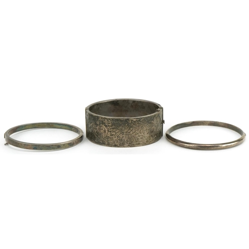 3564 - Three Edwardian and later silver hinged bangles, one with floral chased decoration, total 60.2g