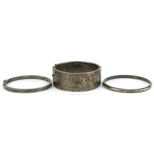 3564 - Three Edwardian and later silver hinged bangles, one with floral chased decoration, total 60.2g