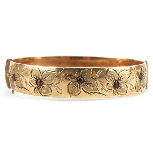 3605 - 9ct rolled gold garnet hinged bangle engraved with flowers, 6.5cm wide, 32.3g