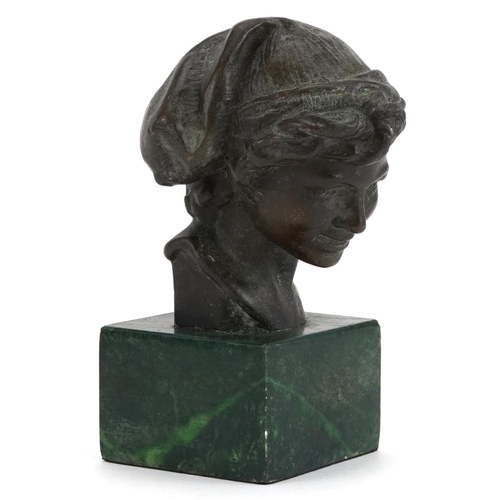 253 - Patinated bronze head and shoulders bust of a young female wearing a hat raised on a green marble ba... 