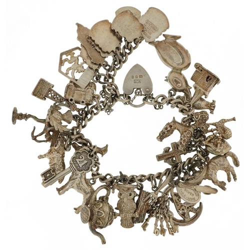 2107 - Heavy silver charm bracelet with a collection of mostly silver charms including Cupid, enamelled sou... 