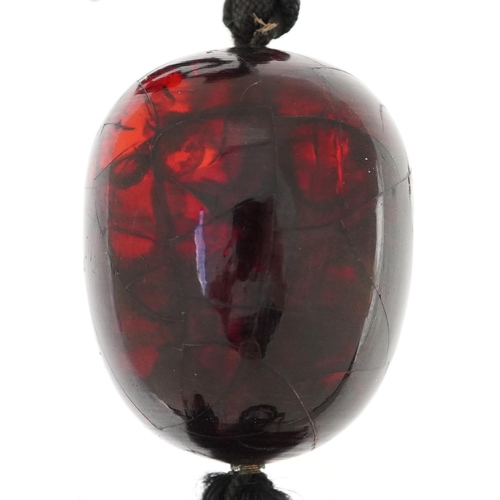 2129 - Large cherry amber coloured bead on a chord necklace, the bead 37mm x 29mm in diameter, total weight... 