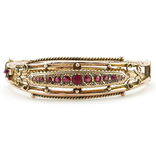 Edwardian 9ct rose gold hinged bangle set with eleven graduated red stones and seed pearls, Chester 1908, 6.5cm wide, 12.5g