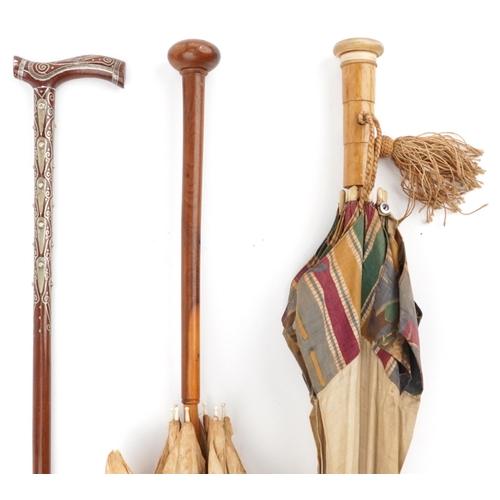 615 - Two early 20th century parasols and a Middle Eastern hardwood walking stick with foliate metal inlay... 