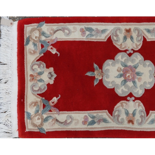 1223 - Three Chinese red ground floral rugs including a runner, the largest 255cm x 70cm