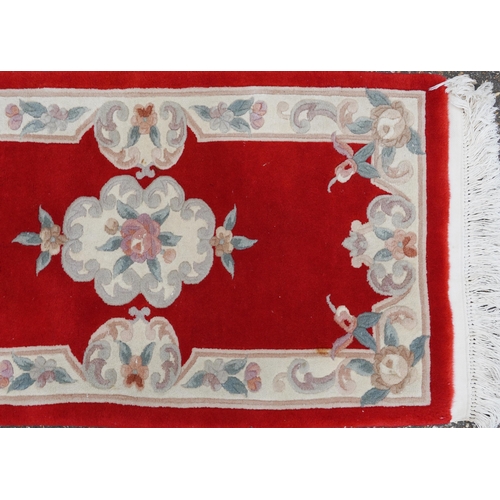 1223 - Three Chinese red ground floral rugs including a runner, the largest 255cm x 70cm