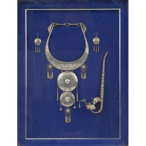 1310 - Thai white metal jewellery and opium pipe housed in a glazed framed display, overall 55cm x 42.5cm