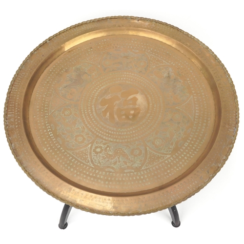 188 - Chinese brass charger engraved with flowers raised on a hardwood table base, 47cm high x 81cm in dia... 