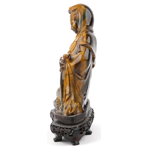 122 - Chinese tiger's eye carving of Guanyin raised on hardwood stand carved with foliage, 16cm high