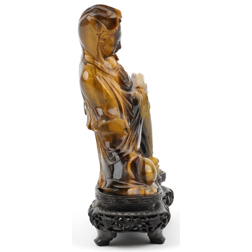 122 - Chinese tiger's eye carving of Guanyin raised on hardwood stand carved with foliage, 16cm high