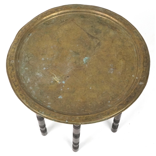 1058 - Middle Eastern brass tray top folding coffee table engraved with foliage, 52cm high x 60cm in diamet... 