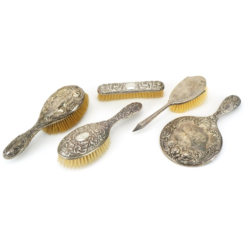 2446 - Four silver backed vanity brushes and a hand mirror, four profusely embossed with foliage, the large... 