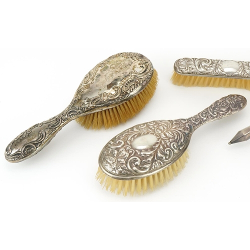 2446 - Four silver backed vanity brushes and a hand mirror, four profusely embossed with foliage, the large... 